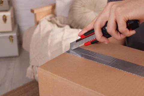 Man using utility knife to open parcel at home, closeup Stock Photos