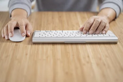 Man using white computer keyboard and mouse on the wooden desk table. Stock Photos