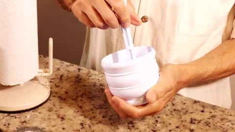 Man using with a white plastic mortar and pestle crushing flax seeds 動画素材 334689597