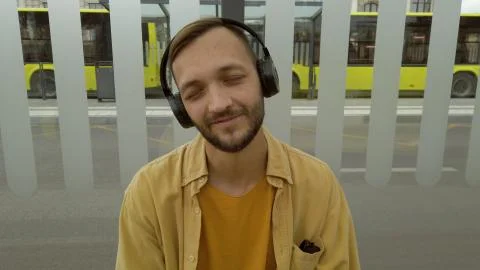 Man using wireless headphones sitting on bus stop.Male enjoying listening music  Stock Photos