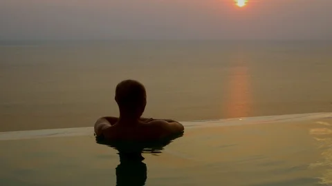A man on vacation enjoys the sunset while in the pool. Stock-Footage 88784848