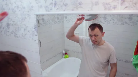 The man is very surprised to see the reflection of his bald head in the mirror Stock Footage 132720460