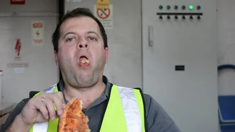 Man in vest eats slice of pizza on workplace Video stock 143448114