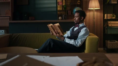 Man in Vest Reading Old Book on Sofa in Cozy Room Stock Footage 306924517