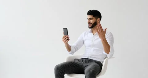Man video chatting using mobile phone against white background Stock Footage 196079080