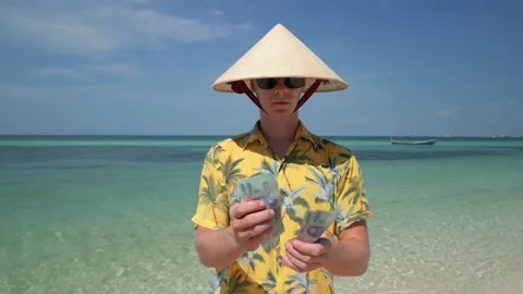 Man in Vietnamese hat counting the Vietnamese Dong on tropical beach in Vietnam 스톡 동영상 259972422