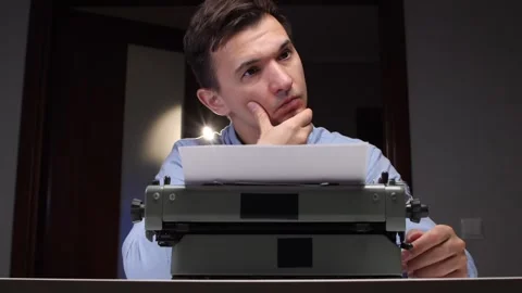Man at vintage typewriter pauses in deep thought, finding inspiration for a Stock Footage 321621596