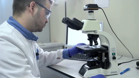 Man virologist is examining virus using microscope at table in pharmaceutical Stock Footage 128297319