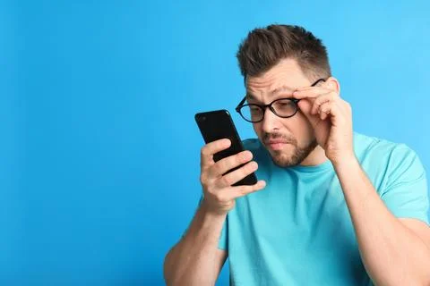 Man with vision problems using smartphone on blue background, space for text Stock Photos