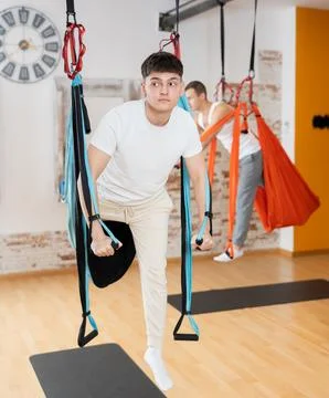 Man visitor performs exercises in hanging position on Pilates slings hammock Stock Photos