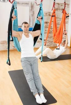 Man visitor performs exercises in hanging position on Pilates slings hammock Stock Photos