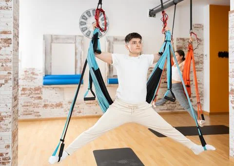 Man visitor performs exercises in hanging position on Pilates slings hammock Stock Photos
