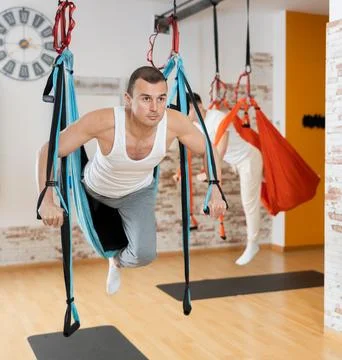 Man visitor performs exercises in hanging position on Pilates slings hammock Stock Photos