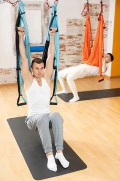 Man visitor performs exercises in hanging position on Pilates slings hammock Stock Photos