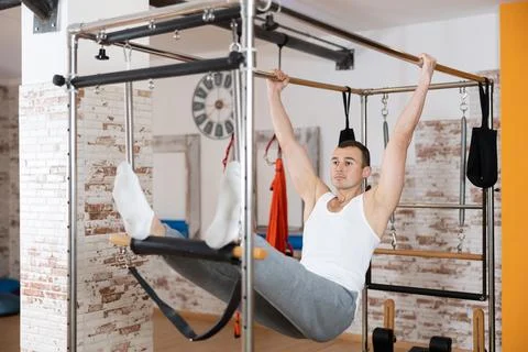Man visitor performs exercises in hanging position on combined Pilates trapeze Stock Photos