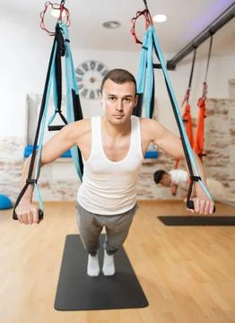 Man visitor performs exercises in hanging position on Pilates slings hammock Stock Photos