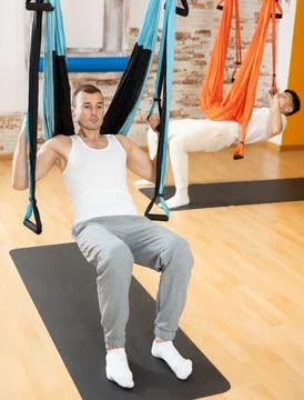 Man visitor performs exercises in hanging position on Pilates slings hammock Stock Photos