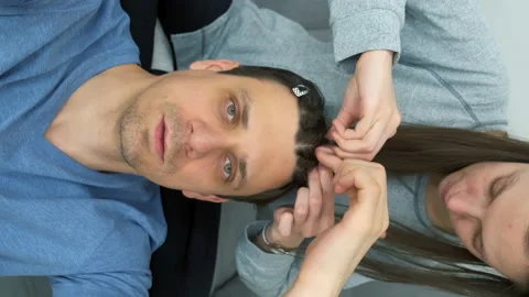 Man vlogger is speaking at camera while woman is doing his hair french braids. Stock Footage 168610414