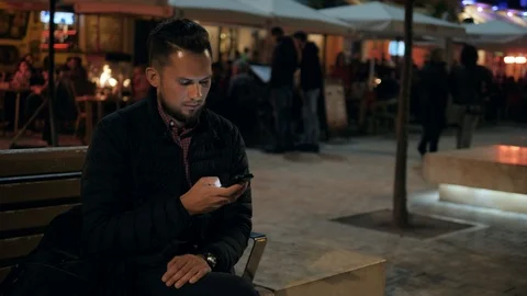 Man voice recognition with smart phone in park on bench night hotel bar outdoor Stock Footage 100579338