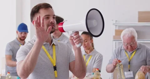 Man volunteer screaming in megaphone working at charity center announcing free Stock Footage 317127743