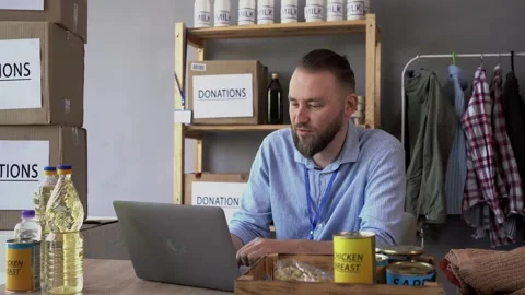 Man volunteer using laptop computer while preparing food for donation box in the Video stock 242078751