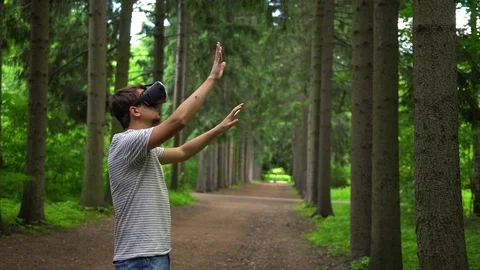 Man in VR goggles tries to touch the objects in virtual reality. Green park as Vídeos de archivo 80130851