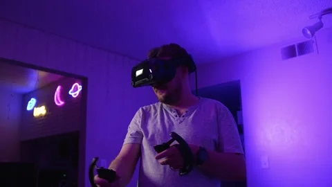 Man in VR headset holding controllers playing virtual reality at home Stock Footage 334090214