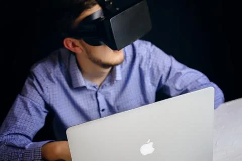 A man in a VR headset sits in front of an Apple laptop 写真素材