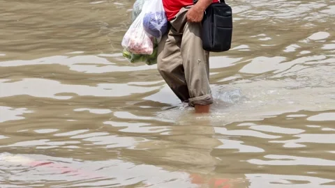 Man wading through a flooded street with shopping bags Stock Footage 345343960