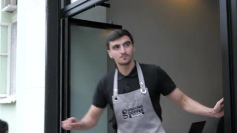 Man waiter in grey apron goes out of cafe on city street Stock Footage 138636498