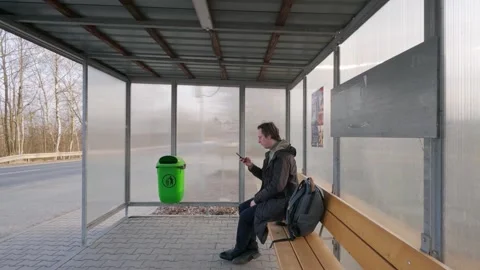 A man waiting at a bus stop dials a number and talks on the phone. Passing the Stockbeeldmateriaal 332813168