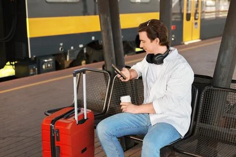 Man waiting on a train station platform with red suitcase luggage. The pass.. Stock Photos