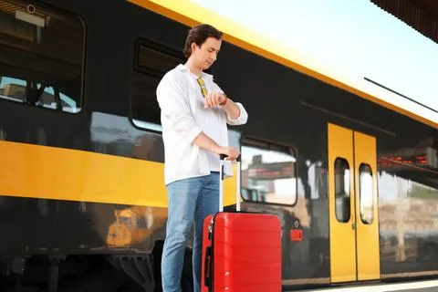 Man waiting on a train station platform, checking his watch while holding a.. Stock Photos