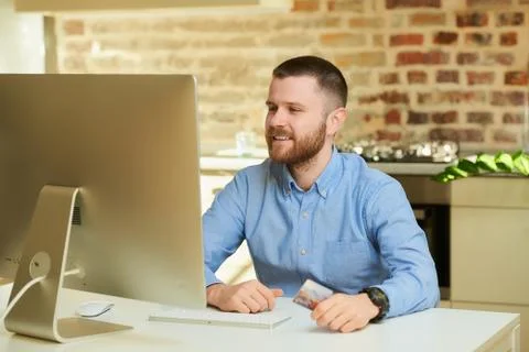 A man waits for an auction in front of the computer and holds a credit card. Stock Photos