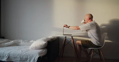 A man wakes up at dawn, gets up, drinks coffee and starts working on a laptop Stock Footage 302901381