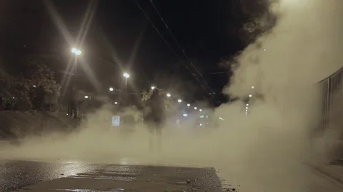 Man walk toward camera in night city street covered in steam from drain accident Stock Footage 73022767