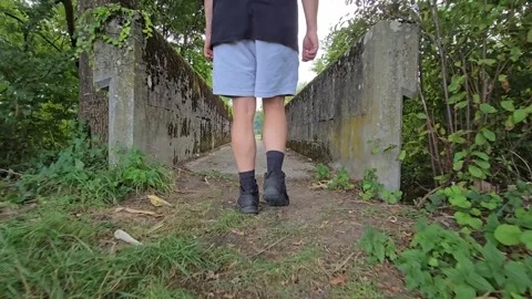 A man is walking across a small concrete with plants overgrown bridge. Stock Footage 346315227