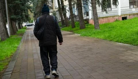 Man walking alone on a quiet path lined with trees in a peaceful neighborho.. Stock Photos