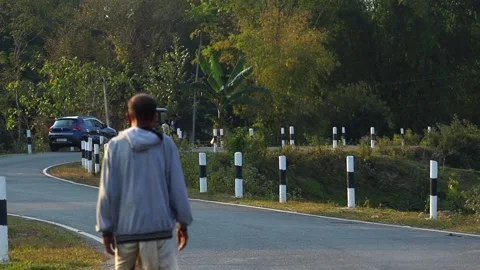 Man walking alone on a rural road surrounded by greenery in Assam Stock Footage 328340703
