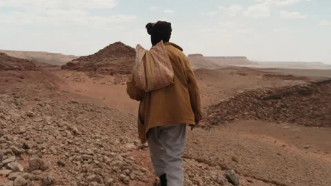 Man walking alone through a vast rocky desert landscape Video stock 343318734