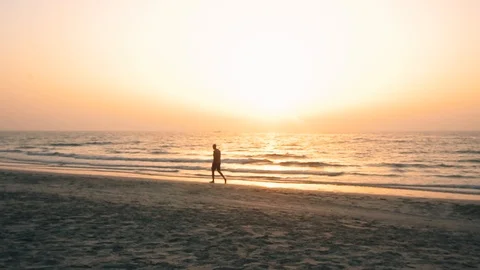 A man is walking along the beach during sunset Stock Footage 99606803