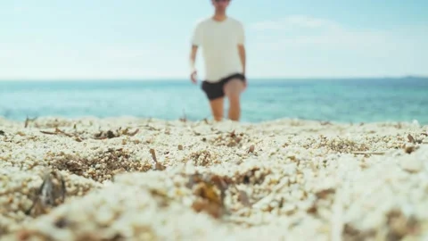 Man is walking along the beach. Young man in a white T-shirt, black shorts and a Stock Footage 154582012