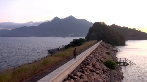 Man walking along dam of plover cover reservoir, alone in sunset 스톡 동영상 144164948