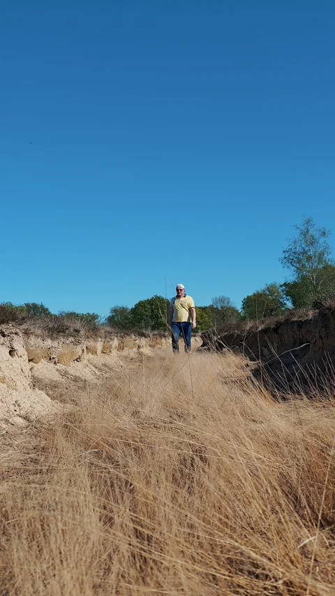 Man walking along dry ditch in Italian nature reserve among wild dry vegetation Stock Footage 332810408