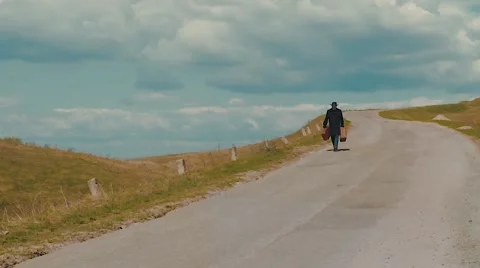 The man walking along the road with two old suitcases on the grass in the summer Stock Footage 63080463