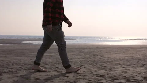 Man walking along a sandy beach at sunset Stock Footage 233985259