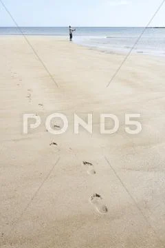 Man walking along shore of beach carrying fishing rod Stock Photos