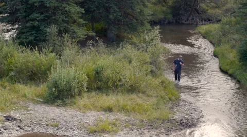 A man walking along a stream or river with a fishing pole in his hand Stock Footage 63117759