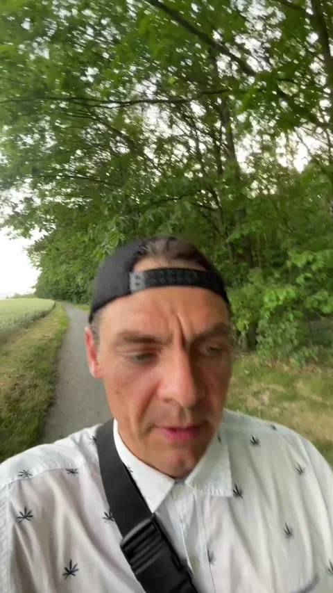 Man walking along tree-lined country path speaking to camera in handheld selfie Stock Footage 344587528