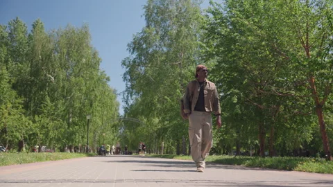 Man walking along tree lined path in bright daylight with residential buildings Stock Footage 345138258